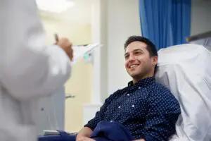 A man sitting in a hospital chair smiling at the camera.